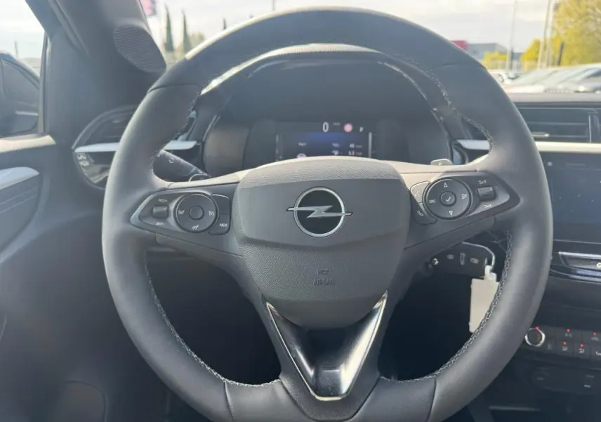 Vue rapprochée du volant noir de l’Opel Corsa 2025 avec commandes intégrées et tableau de bord numérique en arrière-plan.