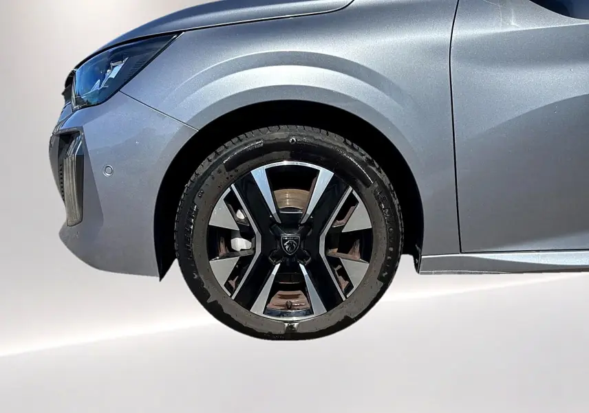 Gros plan sur la roue avant gauche et l'aile d'une Peugeot 208 gris artense avec jante alu au design moderne.