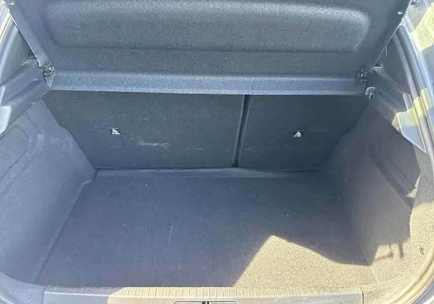 Coffre ouvert en vue plongeante d'une Peugeot 208 gris artense, montrant l'espace de chargement et la banquette arrière rabattable.