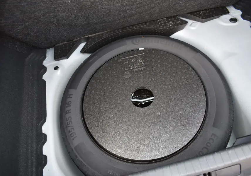Pneu de secours noir dans le coffre d'une Opel Corsa gris 2021, vue en plongée sur la roue de secours.