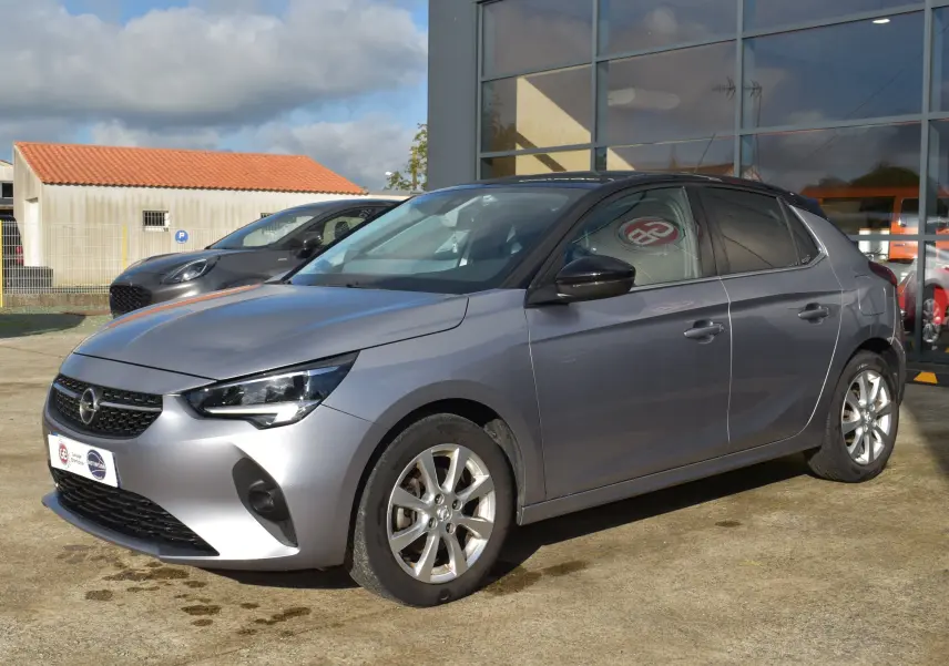 Opel Corsa gris vue 3/4 avant droit, avec jantes alliage et calandre noire brillante sous un ciel partiellement nuageux.