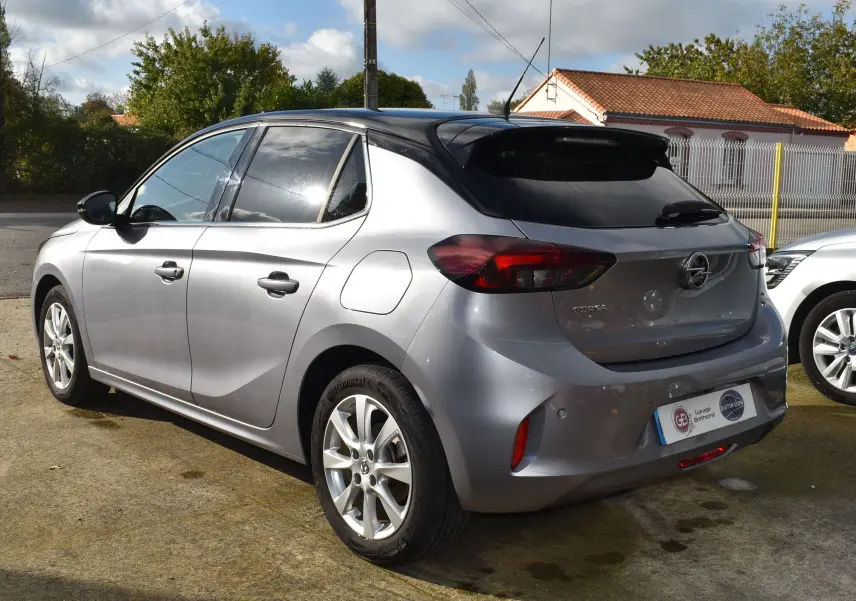 Opel Corsa gris vue 3/4 arrière côté gauche, avec toit noir et feux arrière foncés, stationnée en extérieur.