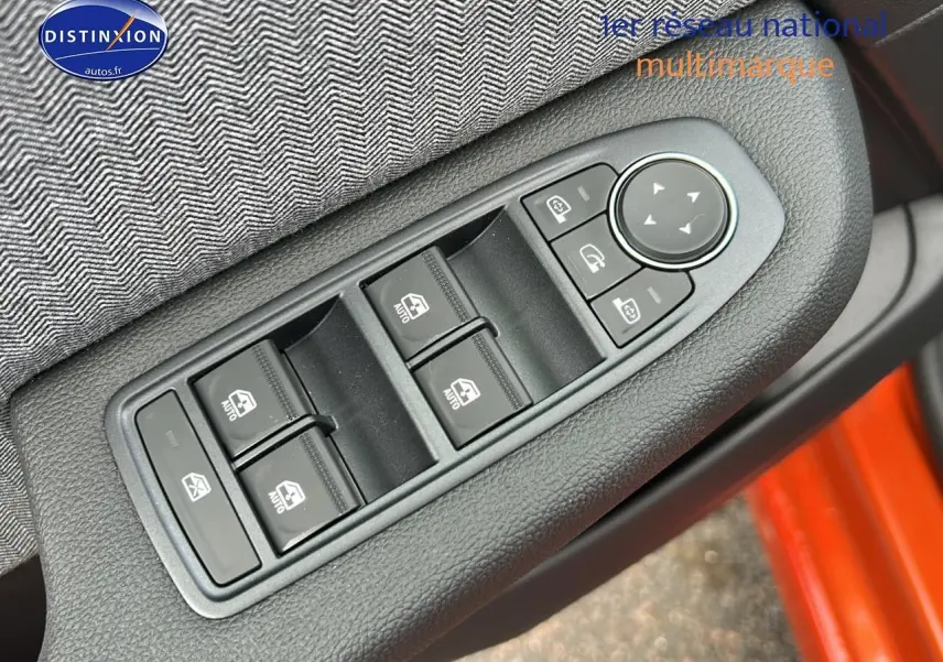 Gros plan sur les commandes des vitres et rétroviseurs côté conducteur d'une Renault Clio V orange Valencia.