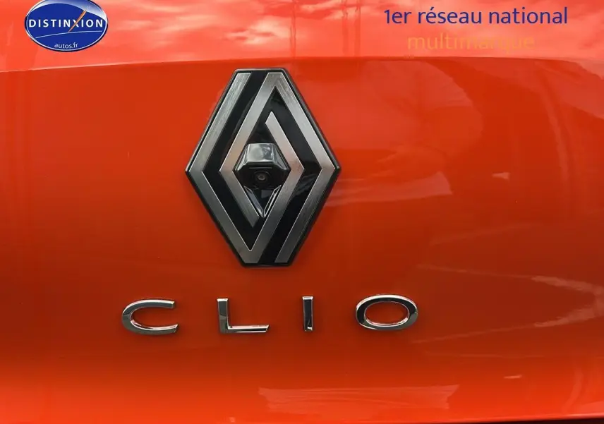Gros plan sur le logo Renault et le badge Clio sur la malle arrière orange Valencia d'une Clio V hybride.
