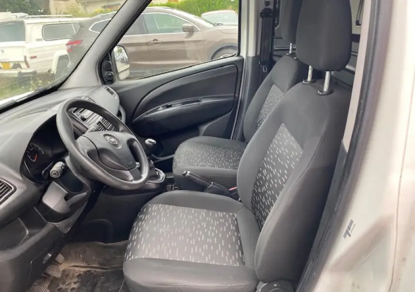 Vue intérieure côté conducteur de l'Opel Combo blanc 2016, montrant sièges tissu gris et tableau de bord simple.