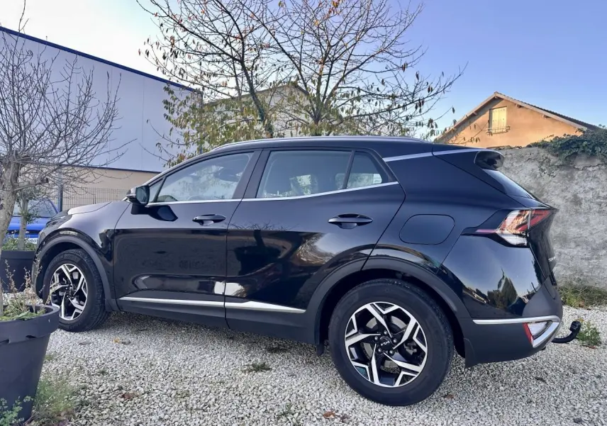 KIA SPORTAGE noir vu de profil côté gauche, avec jantes alliage et attelage de remorque visible à l'arrière.