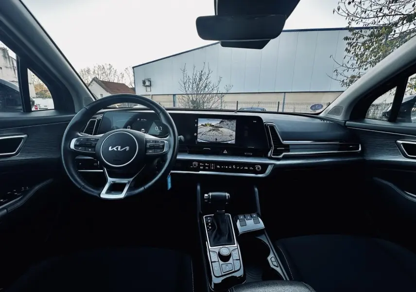 Intérieur noir du Kia Sportage 2023 vu de face, avec tableau de bord moderne et écran tactile affichant la caméra de recul.