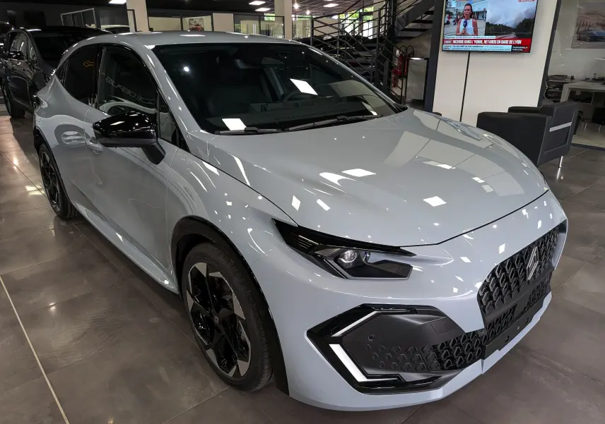 Renault Clio VI TCe 115 Gris Rafale vue 3/4 avant droit en showroom, avec jantes noires et détails noirs contrastants.