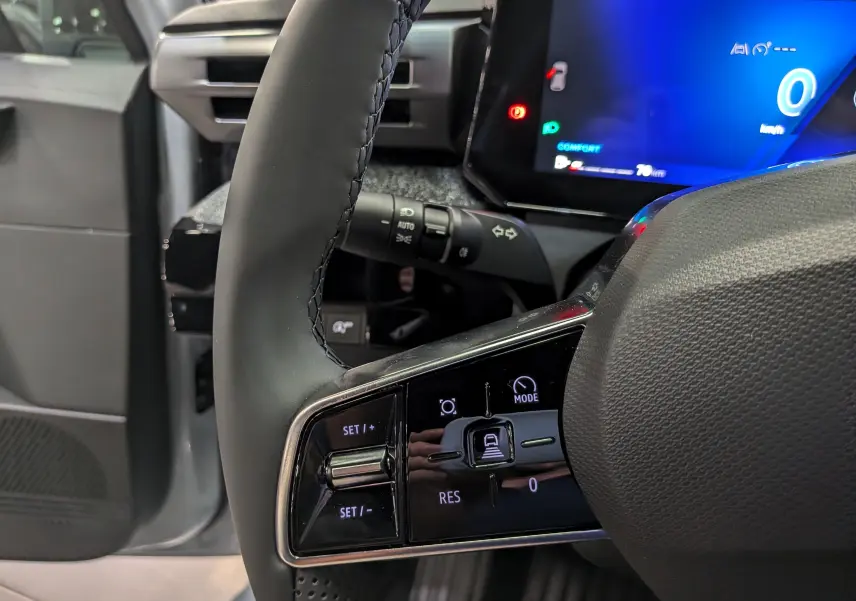 Gros plan sur le volant noir de la Renault Clio VI Gris Rafale, avec commandes de régulateur et écran digital bleu en arrière-plan.