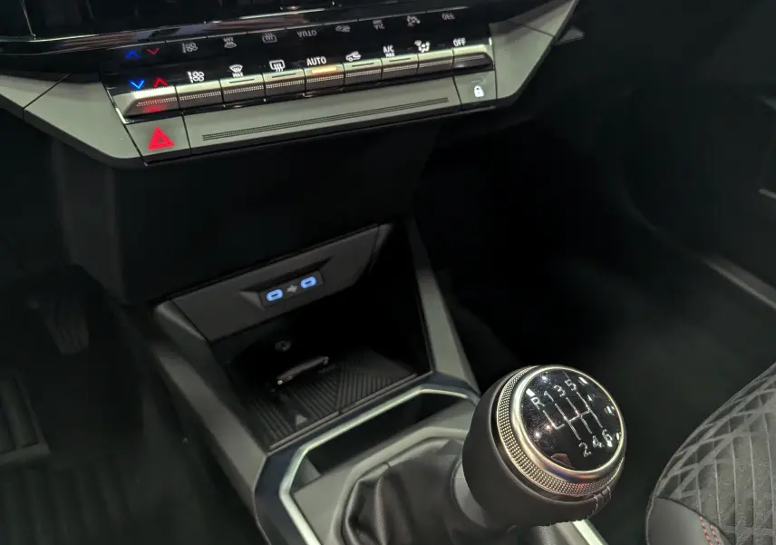 Gros plan sur la boîte manuelle et la console centrale noire de la Renault Clio VI TCe 115 Gris Rafale, avec commandes climatisation.