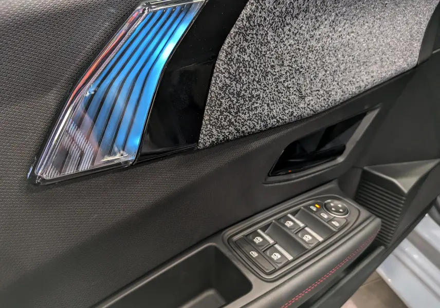 Détail de la porte côté conducteur de la Renault Clio VI TCe 115 Gris Rafale, avec commandes de vitres et insert décoratif bleu.