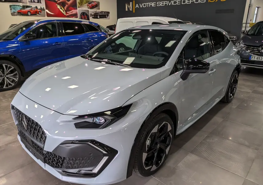 Renault Clio VI TCe 115 Gris Rafale vue 3/4 avant droit en intérieur, avec jantes noires et détails noirs contrastants.