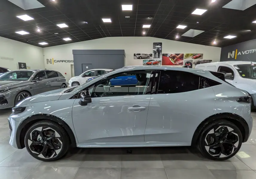 Profil côté gauche de la Renault Clio VI TCe 115 CH TECHNO gris Rafale avec jantes biton et vitres teintées en showroom.