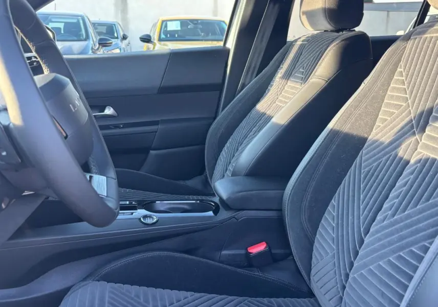 Vue intérieure côté conducteur de la Lancia Ypsilon 2025, sièges en tissu gris avec motifs géométriques et volant sport.