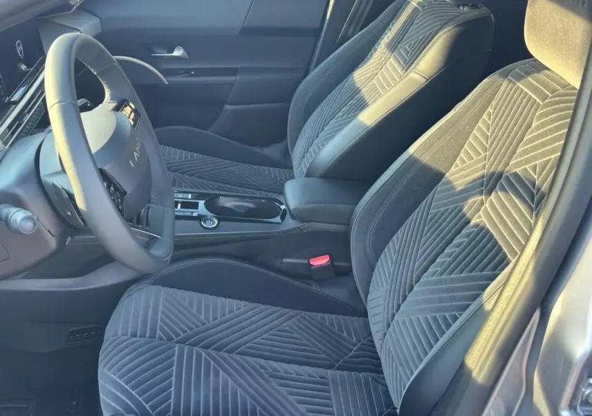 Vue intérieure côté conducteur de la Lancia Ypsilon gris 2025, mettant en valeur les sièges en tissu à motifs géométriques et le volant sport.
