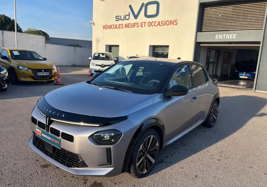 Lancia Ypsilon gris vue 3/4 avant droit, avec jantes 17 pouces et toit noir brillant, stationnée devant un garage.