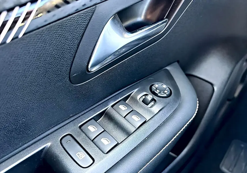 Gros plan sur la commande des vitres électriques côté gauche d’une Peugeot 208 gris selenium, intérieur noir.
