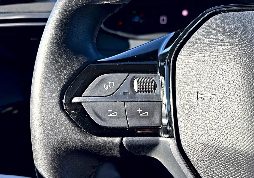 Gros plan sur les commandes gauche du volant noir de la Peugeot 208 1.2 100 Allure gris selenium, boutons de volume et appel mains-libres.