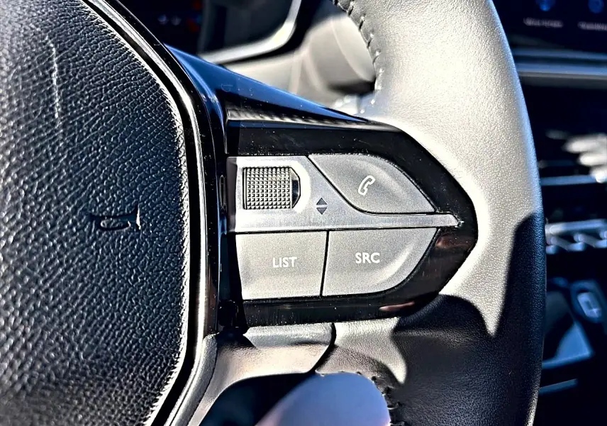Gros plan sur les commandes audio au volant noir du Peugeot 208 1.2 100 Allure, intérieur lumineux.