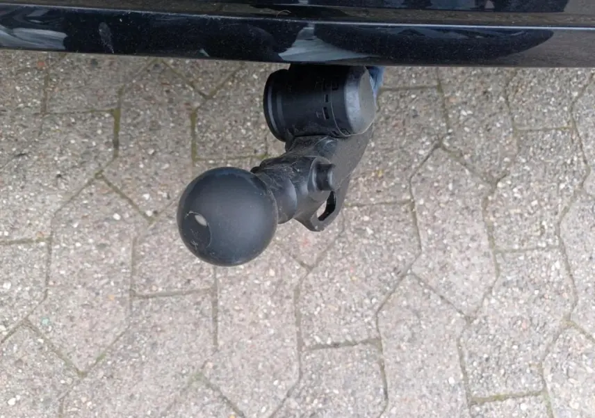 Gros plan sur l'attelage escamotable noir sous le pare-chocs arrière d'une Volkswagen Golf noire métallisée.