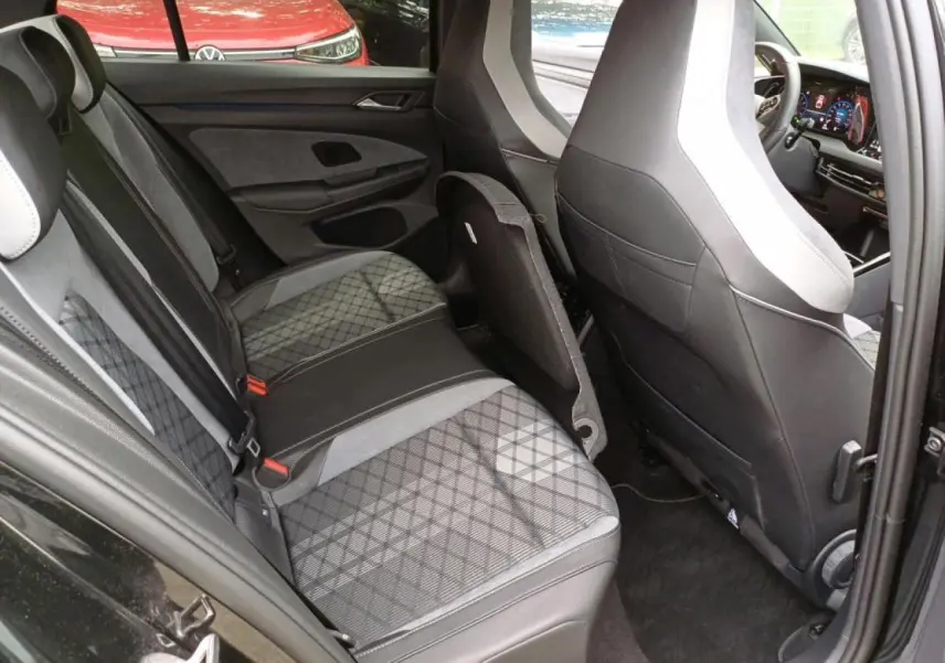 Vue intérieure côté arrière gauche de la Volkswagen Golf noire avec sièges arrière en tissu à motif losanges et cuir noir.