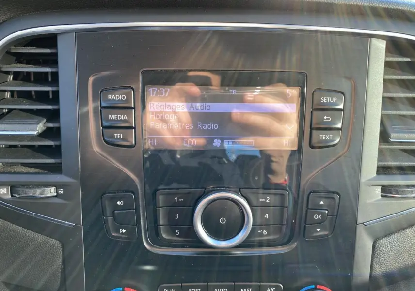 Gros plan sur la console centrale de la Renault Mégane gris platine, affichant l'écran radio et les commandes de climatisation.