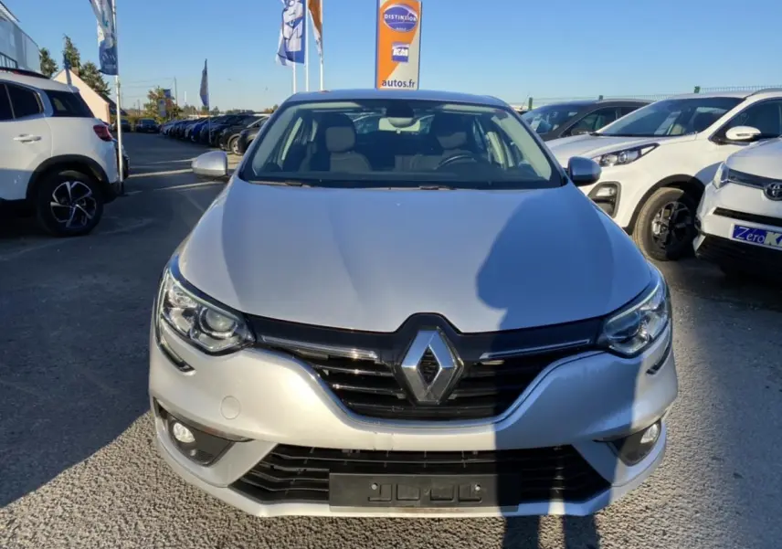 Vue de face d'une Renault Mégane Sedan gris platine avec projecteurs antibrouillard et calandre noire brillante.