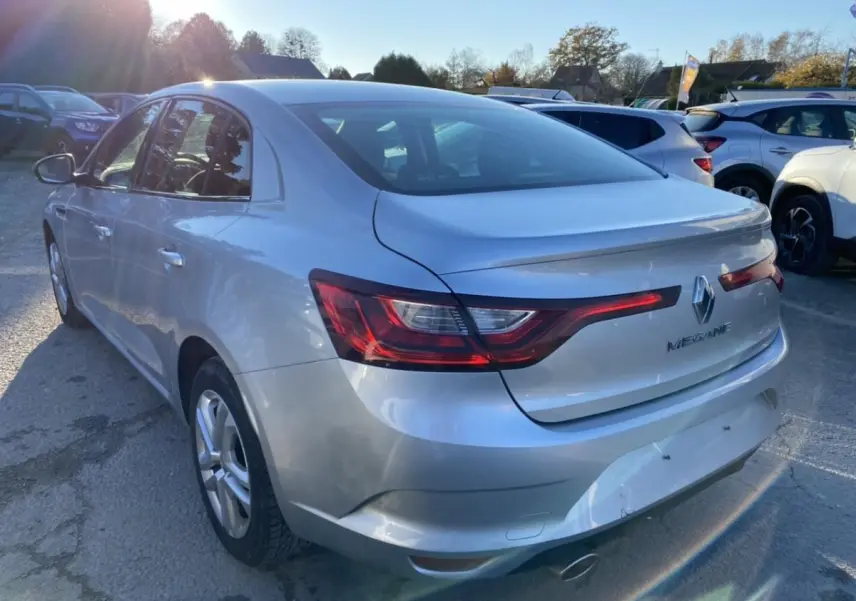 Vue 3/4 arrière droite d'une Renault Mégane Sedan gris platine avec feux arrière allongés et logo Renault visible.