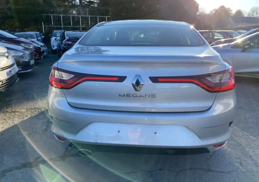 Vue arrière d'une Renault Mégane gris platine avec feux arrière allumés, stationnée en extérieur au soleil.