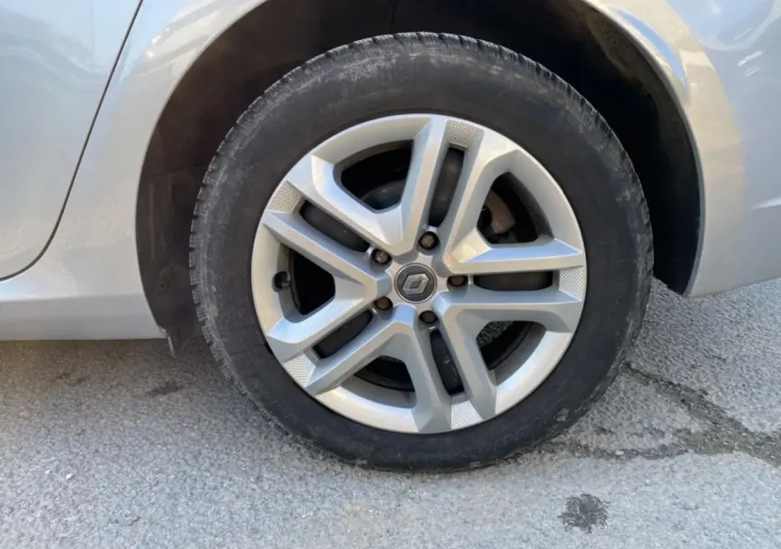 Gros plan sur la roue avant gauche d'une Renault Mégane gris platine, mettant en valeur la jante alliage au design moderne.