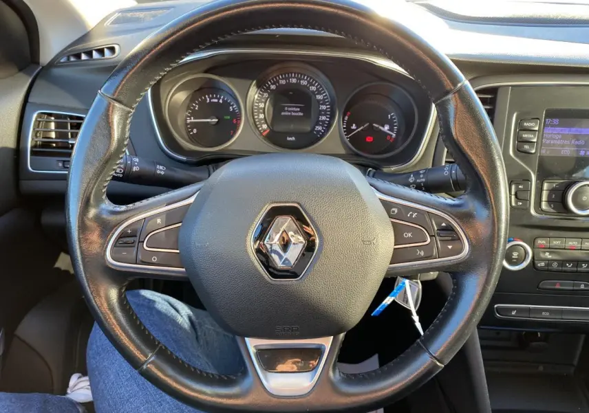 Vue rapprochée du volant en cuir noir avec logo Renault, tableau de bord et console centrale d'une Mégane gris platine 2017.