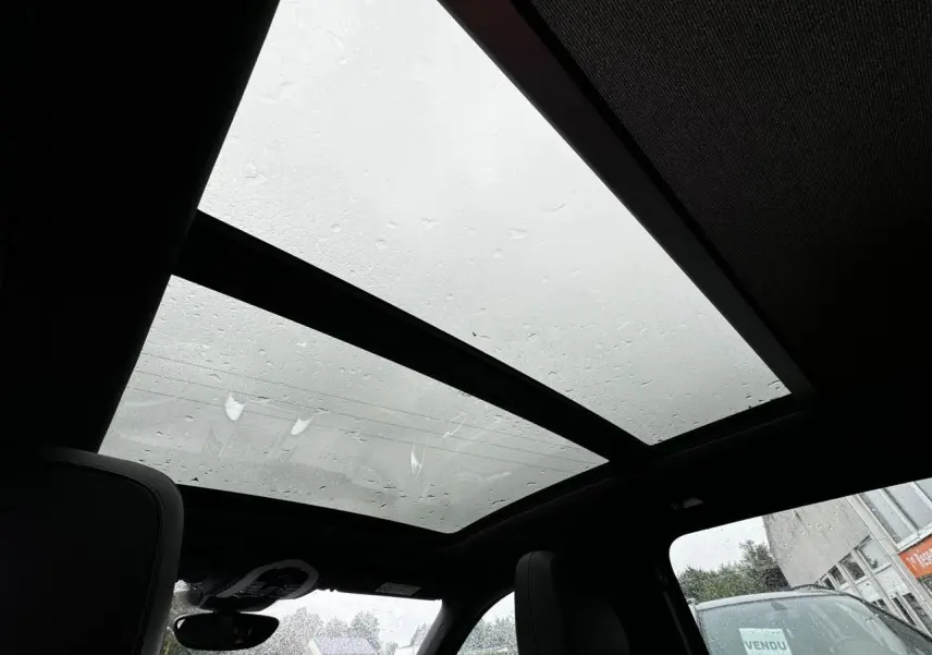 Toit ouvrant panoramique vu de l'intérieur du Porsche Cayenne noir, avec pluie visible sur le verre et sièges en cuir.