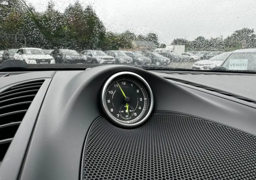 Gros plan sur le chronomètre analogique noir du tableau de bord d'un Porsche Cayenne noir, pluie visible à l'extérieur.