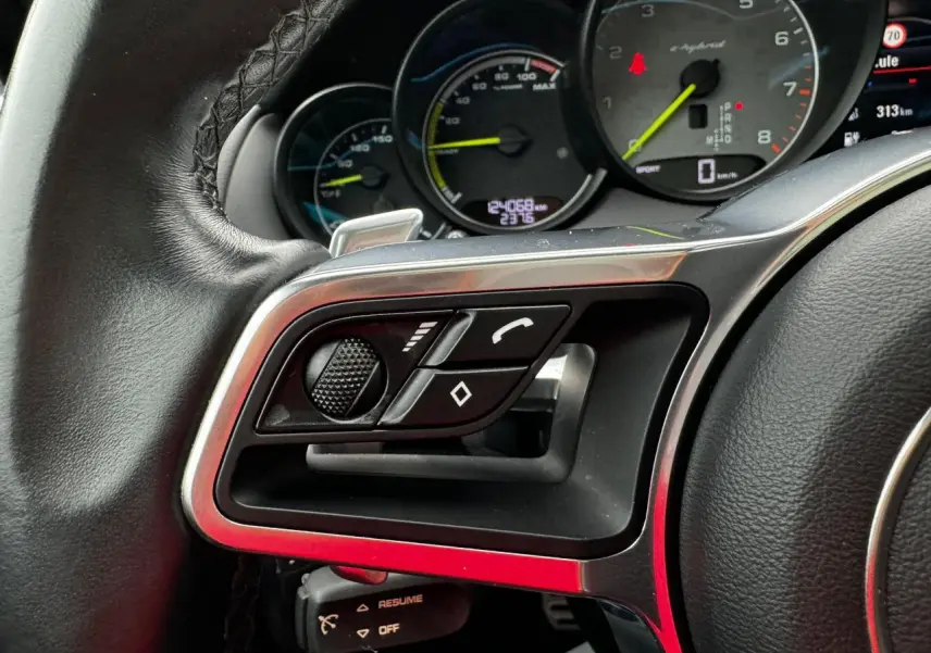 Gros plan sur la partie gauche du volant cuir du Porsche Cayenne 2017 avec commandes multifonctions et compte-tours e-hybrid.