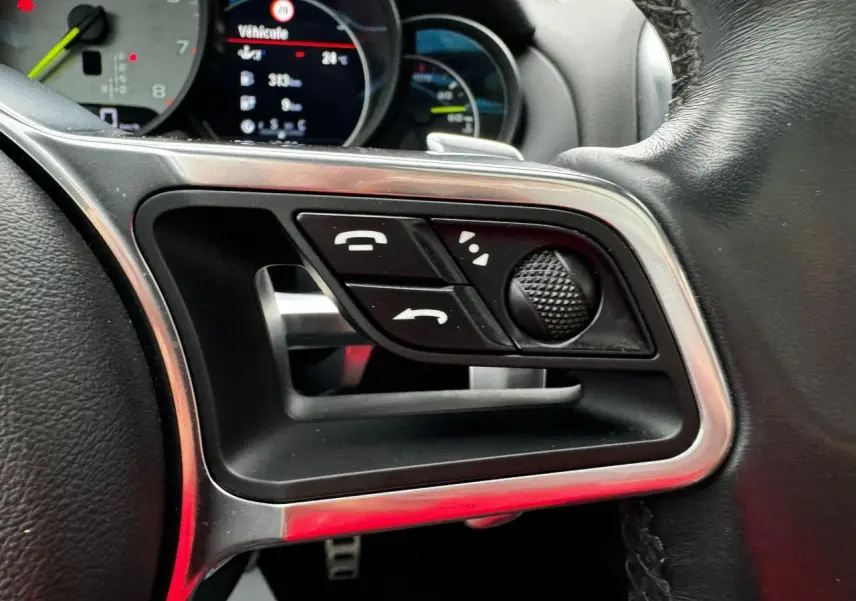 Gros plan sur les commandes du volant cuir noir du Porsche Cayenne S E-Hybrid 2017 avec affichage numérique en arrière-plan.