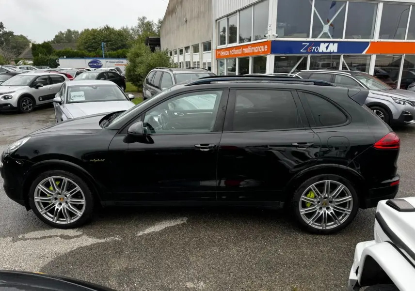 Profil côté gauche d'un Porsche Cayenne noir avec jantes 21 pouces et étriers de frein verts acide sur parking.