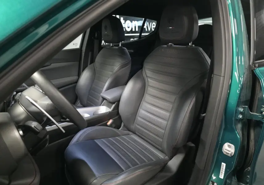 Vue intérieure côté conducteur de l'Alfa Romeo Tonale 2024, sièges sport cuir noir avec surpiqûres rouges, portière verte ouverte.