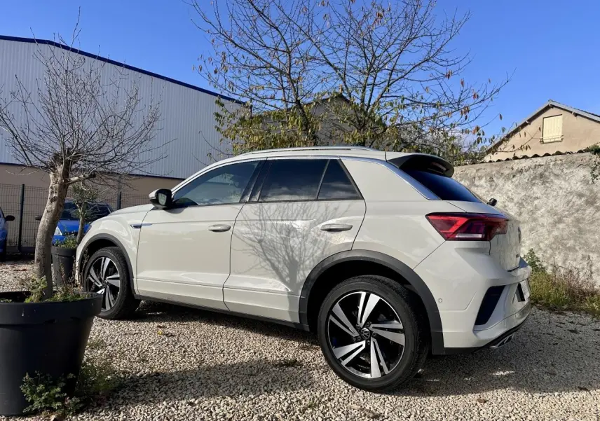 Volkswagen T-Roc gris clair vu de profil côté gauche, avec jantes alliage noires et toit contrasté noir.
