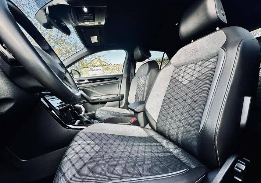 Vue intérieure côté conducteur du Volkswagen T-Roc 2024, sièges R-Line en tissu noir et gris avec motifs géométriques.