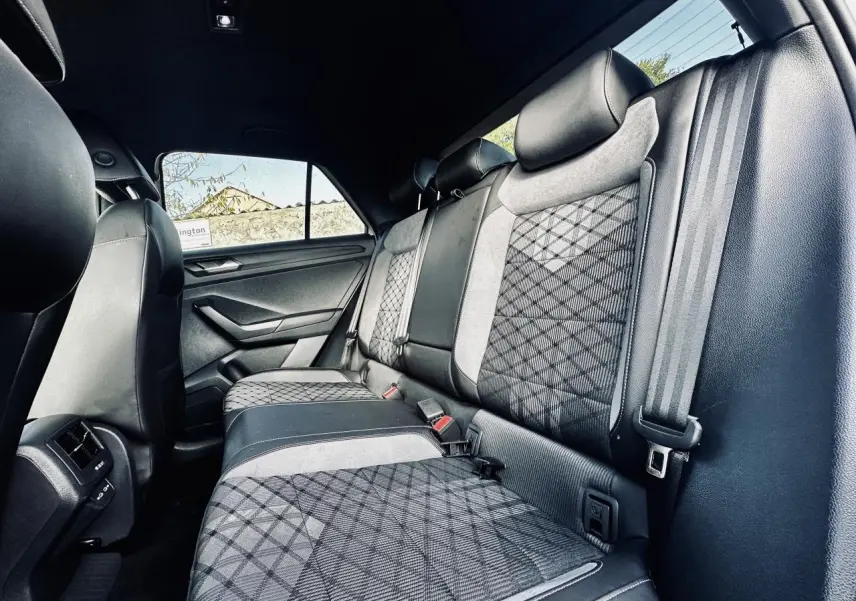 Vue intérieure arrière du Volkswagen T-Roc 2024, sièges arrière gris à motifs géométriques et ceintures de sécurité visibles.