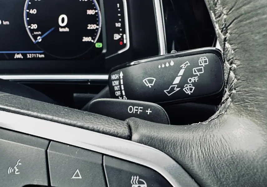 Gros plan sur le volant cuir noir et manette d'essuie-glace du Volkswagen T-Roc gris, tableau de bord digital en arrière-plan.