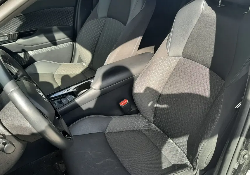 Intérieur avant droit du Toyota C-HR 1.8 Hybrid 2023 noir, sièges tissu noir avec motifs géométriques et console centrale brillante.