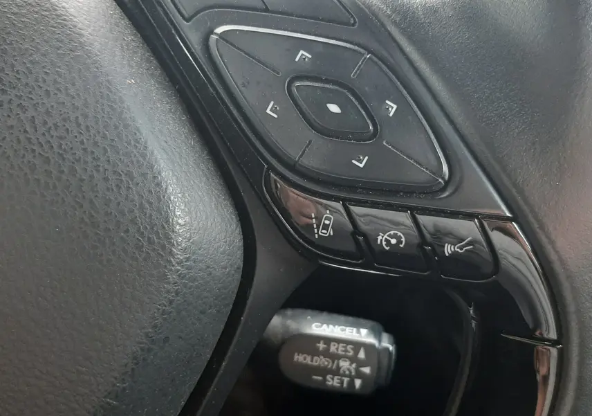Gros plan sur les commandes multifonctions noires du volant côté gauche du Toyota C-HR 1.8 Hybrid 2023.