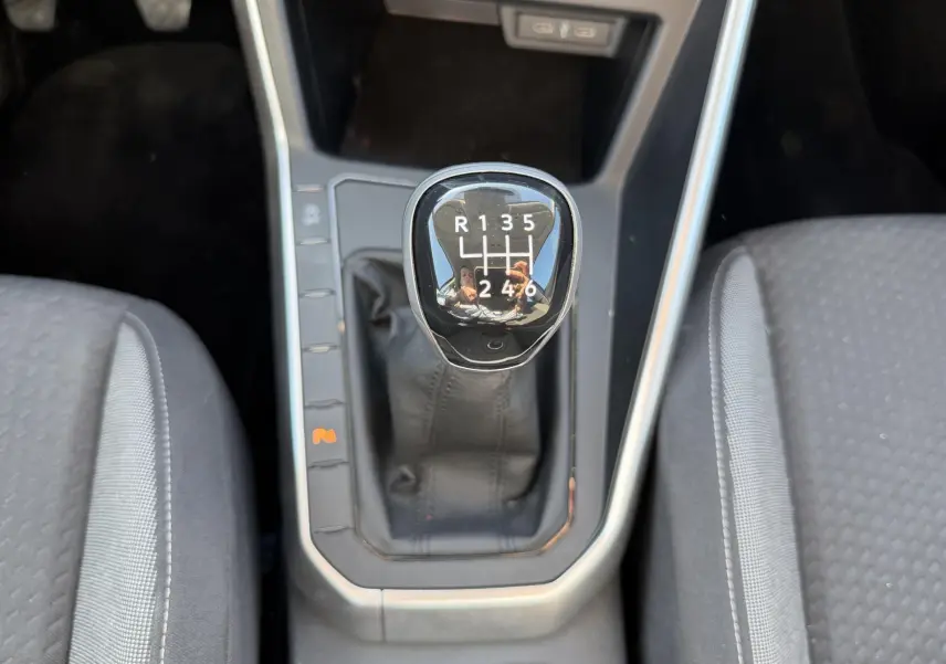 Gros plan sur le levier de vitesse manuel noir entouré des sièges avant gris du Volkswagen Taigo.