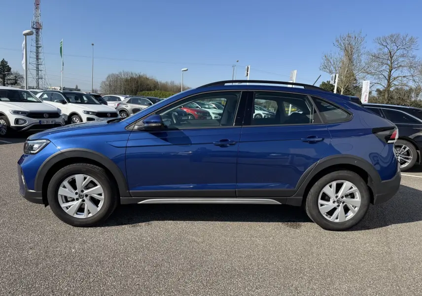 Vue de profil côté gauche d'un Volkswagen Taigo bleu métallisé avec jantes alliage et barres de toit noires.