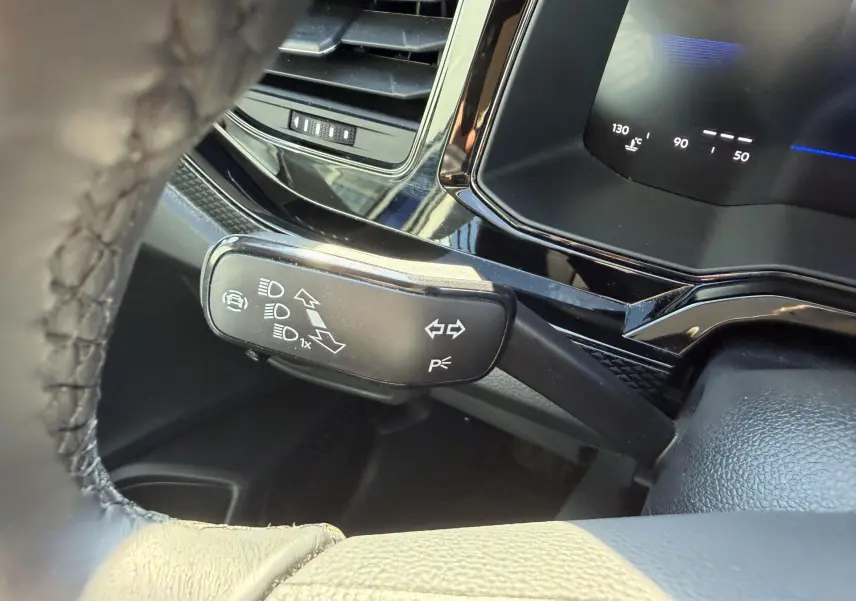 Gros plan sur le commodo gauche du volant cuir du Volkswagen Taigo bleu, avec tableau de bord digital en arrière-plan.