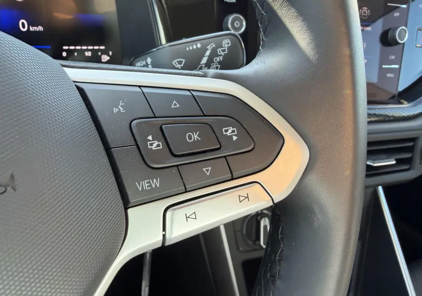 Gros plan sur les commandes du volant cuir noir du Volkswagen Taigo 2025 avec écran digital en arrière-plan.