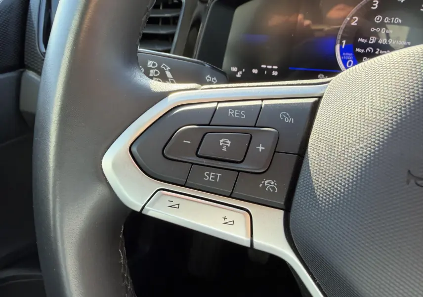 Gros plan sur les commandes du volant cuir à gauche du Volkswagen Taigo 2025, affichage digital en arrière-plan.