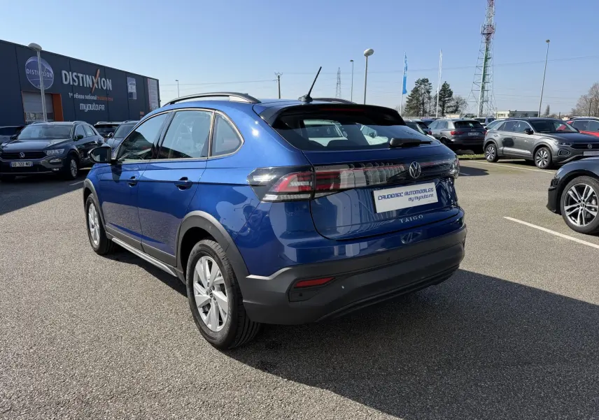 Vue 3/4 arrière droite d'un Volkswagen Taigo bleu métallisé avec barres de toit et feux arrière LED.