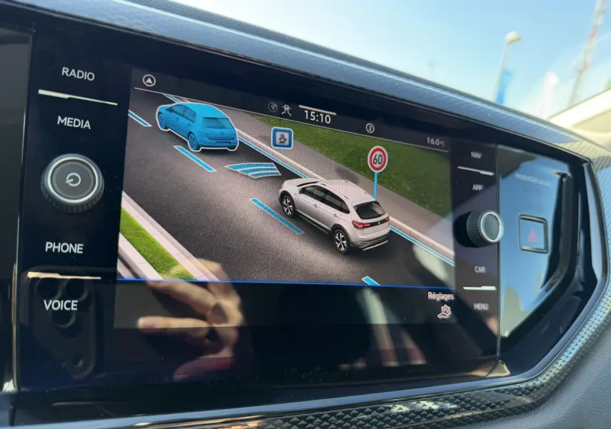 Écran tactile intérieur montrant l'interface d'aide à la conduite avec véhicule blanc et signalisation 60 km/h.